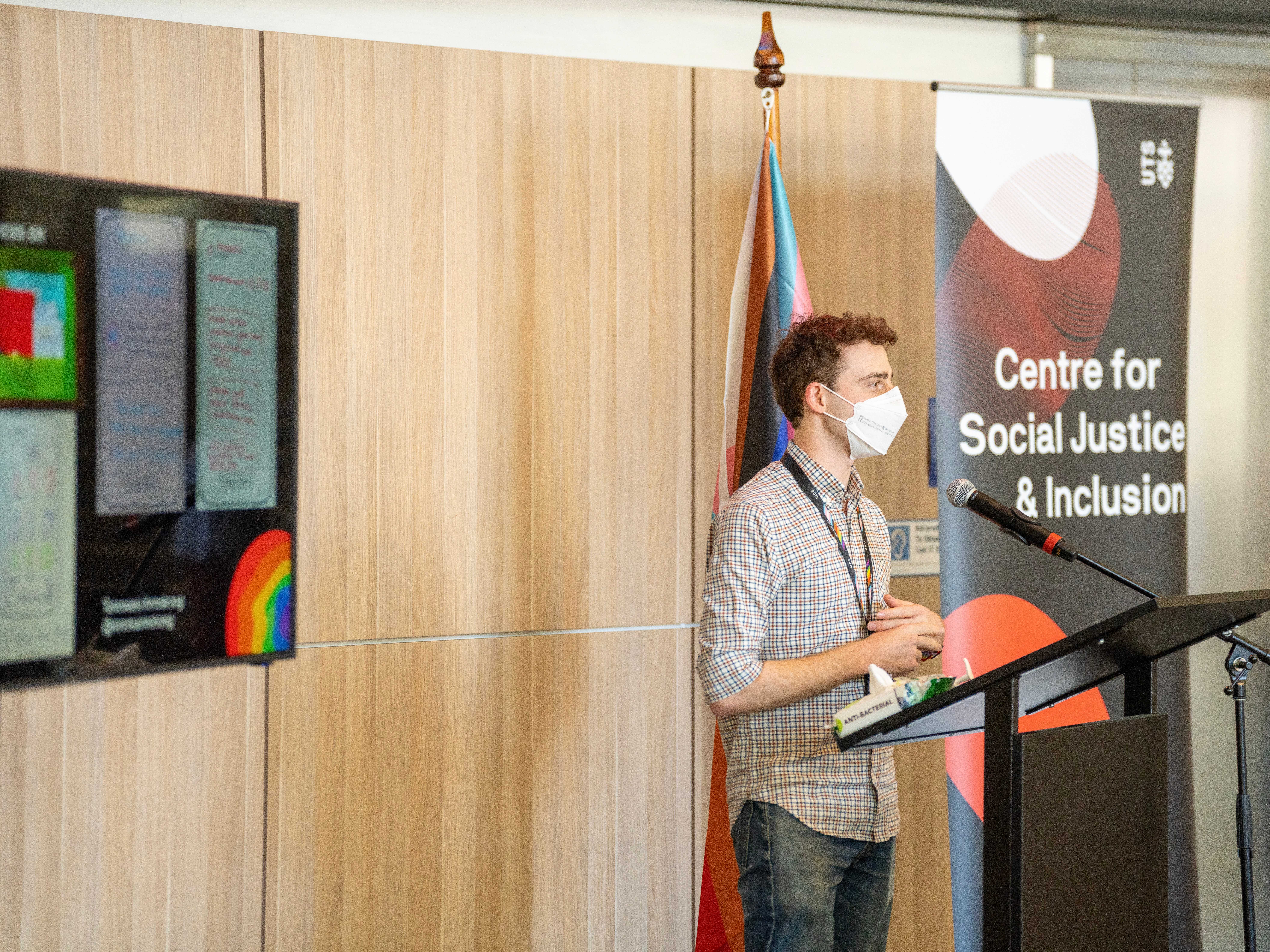 Me standing at a lectern presenting my work. Behind is a banner for the UTS Centre for Social Justice & Inclusion.